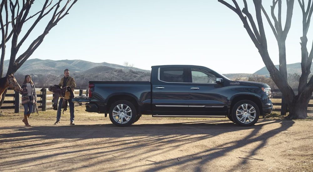 A man is putting a saddle in the bed of a blue 2024 Chevy Silverado 1500 High Country.