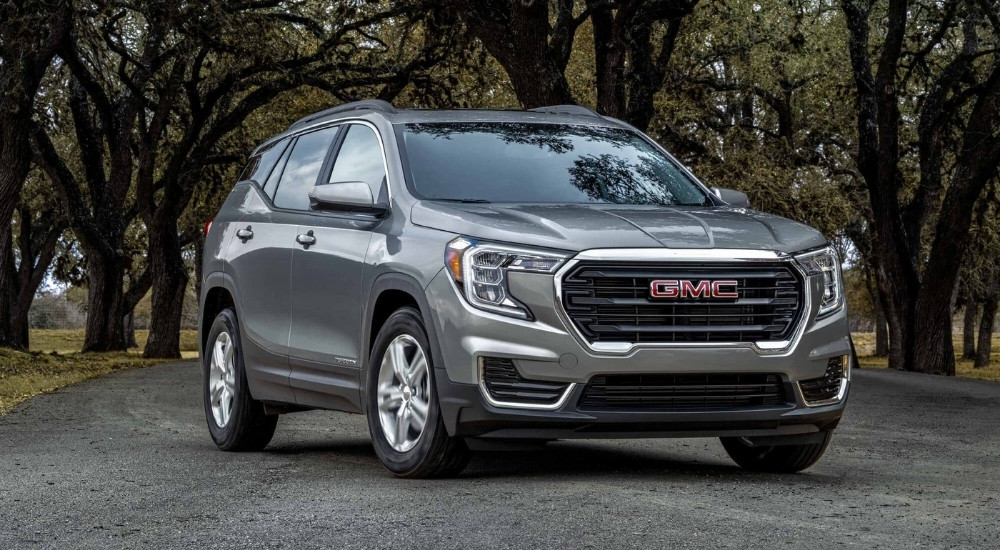 A grey 2024 GMC Terrain for sale is shown on a tree-lined path.