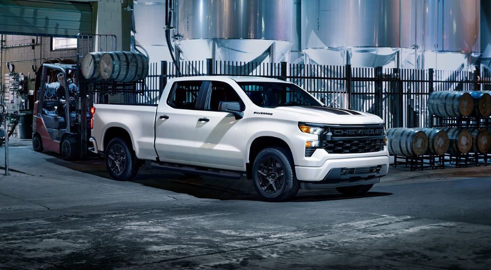 A white 2025 Chevy Silverado 1500 Custom Rally for sale is parked in a city at night.