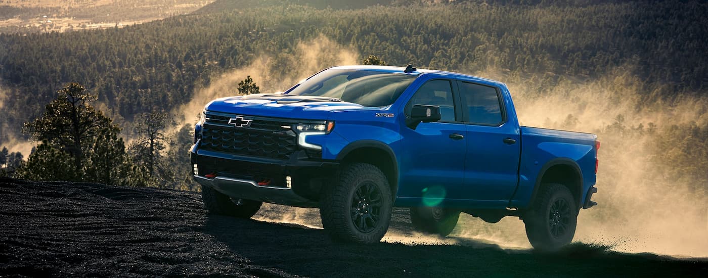 Blue 2025 Chevy Silverado 1500 ZR2 driving off-road on a hill.
