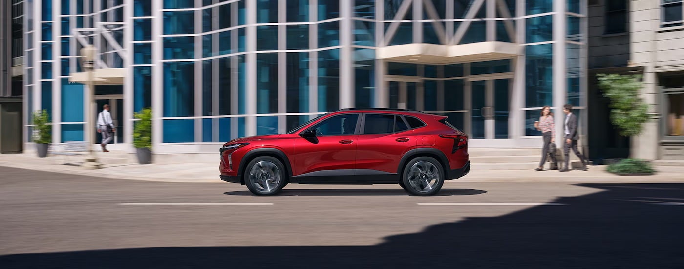 Side of a red 2025 Chevy Trax driving down a road.
