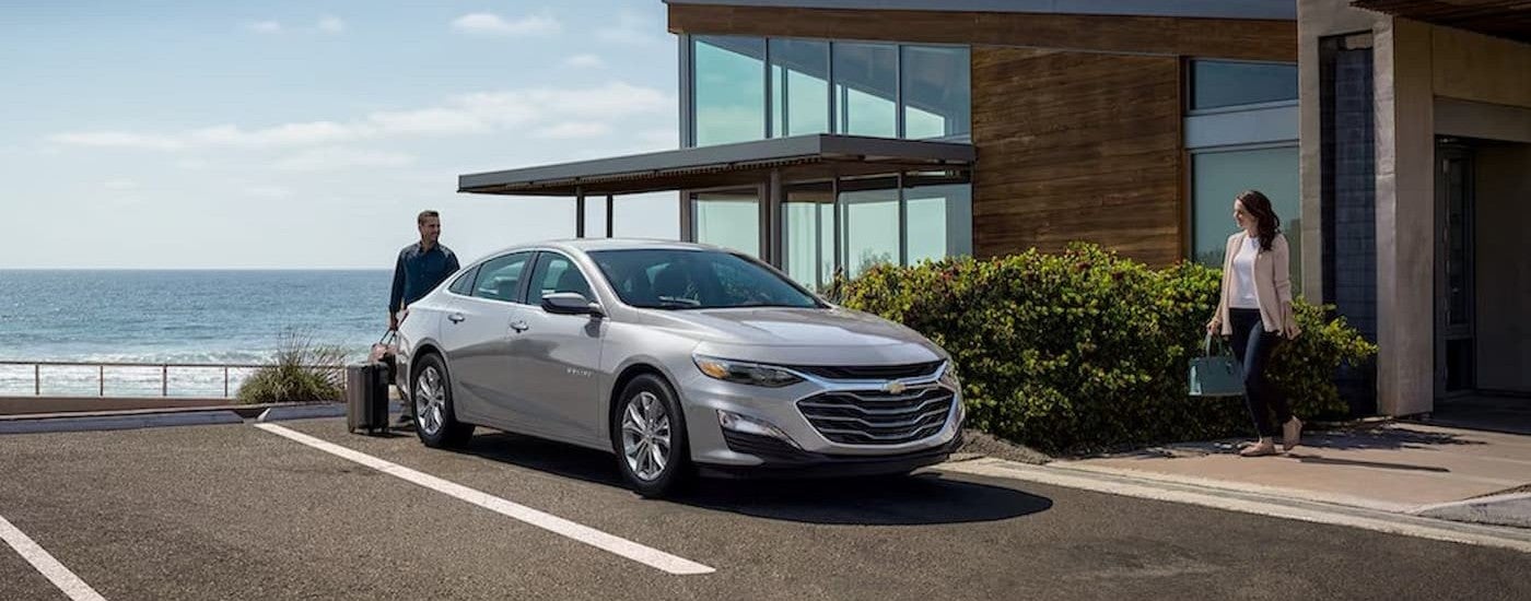 A silver 2025 Chevy Malibu parked near an ocean.