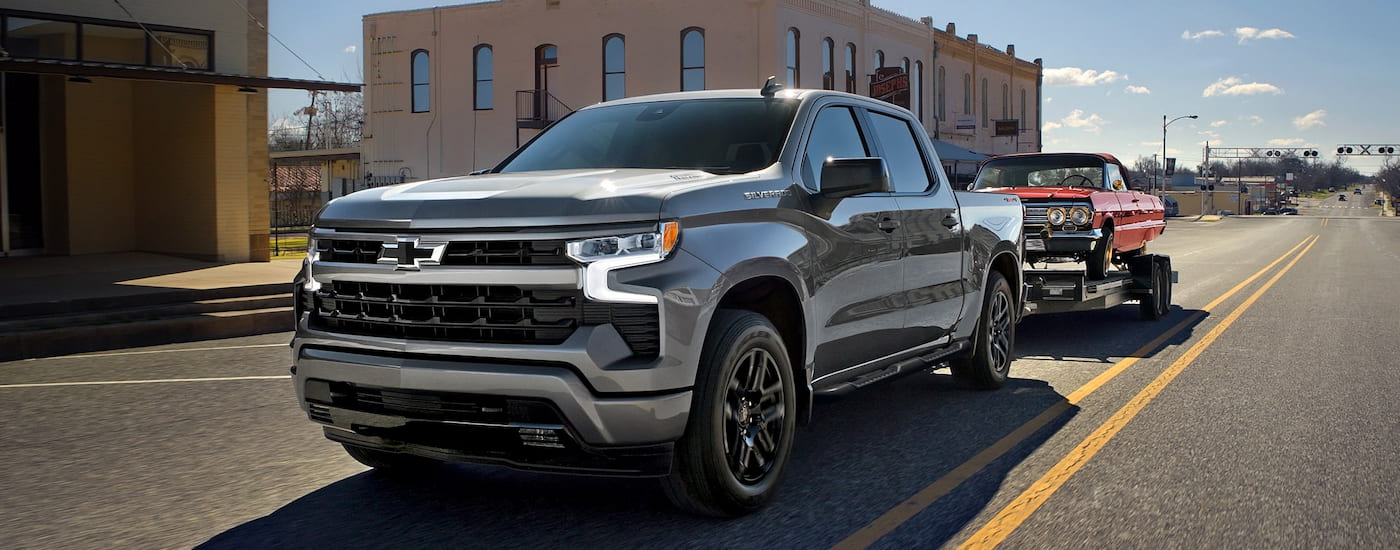 A silver 2025 Chevy Silverado 1500 for sale near Clarksville towing a red car down an open road.