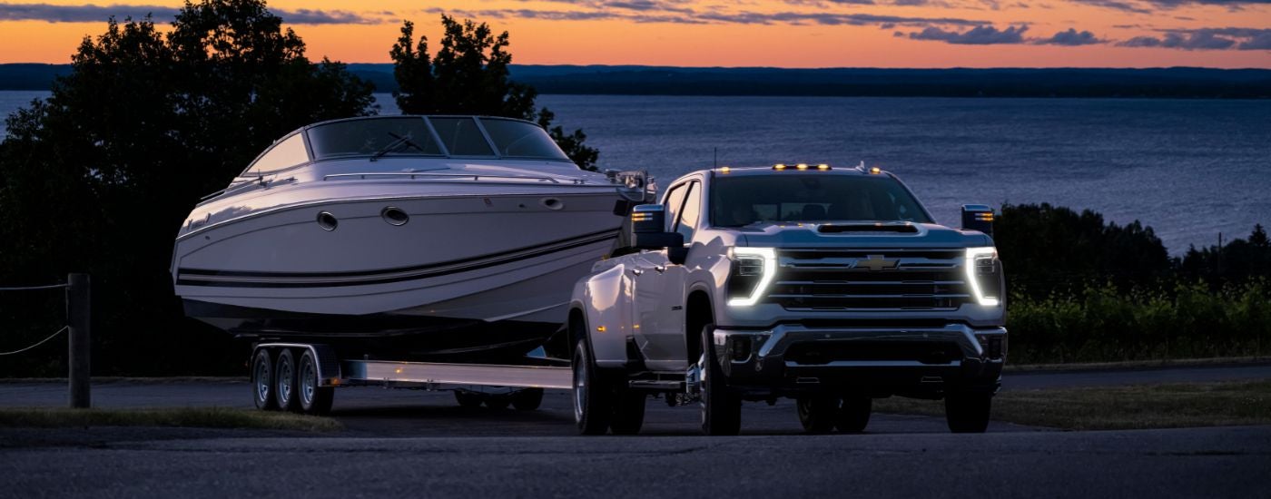 A white 2024 Chevy Silverado 3500 HD LTZ is shown towing a boat.
