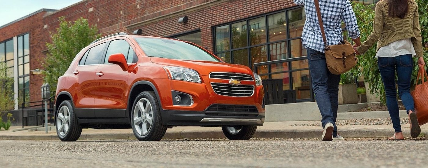 People are walking past a red/orange 2016 Chevy Trax.