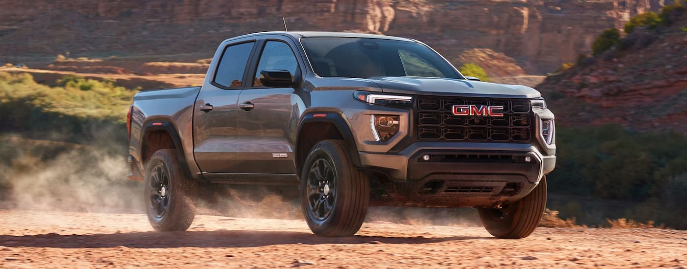 Silver 2025 GMC Canyon driving down a dirt road.