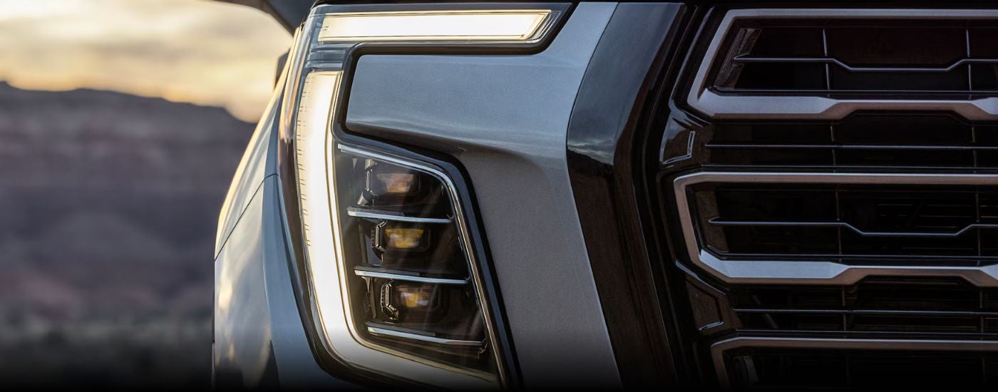 A close up shows the grille and headlight on a silver 2025 GMC Yukon.