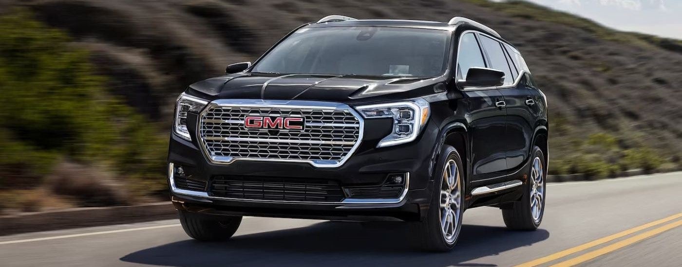 A black 2024 GMC Terrain for sale is driving on an open road.