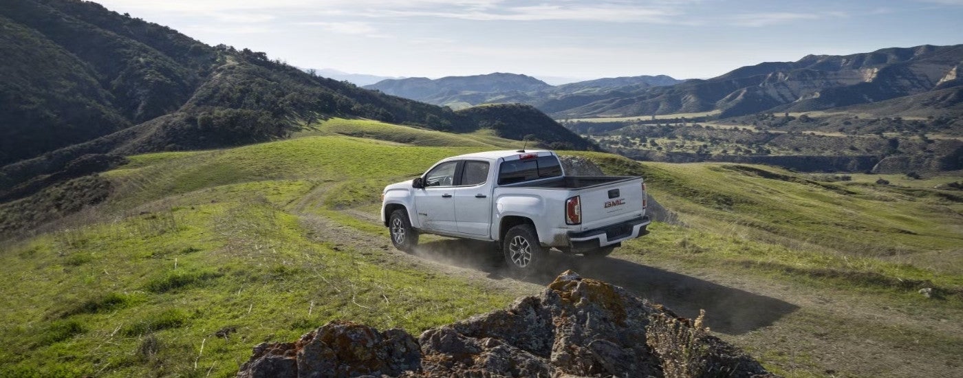 A white 2022 GMC Canyon AT4 is driving on a dusty dirt road.