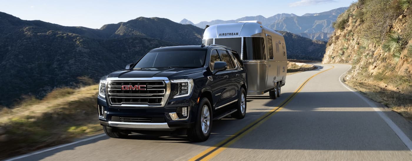 A black 2022 GMC Yukon is towing a silver camper on a mountain highway.